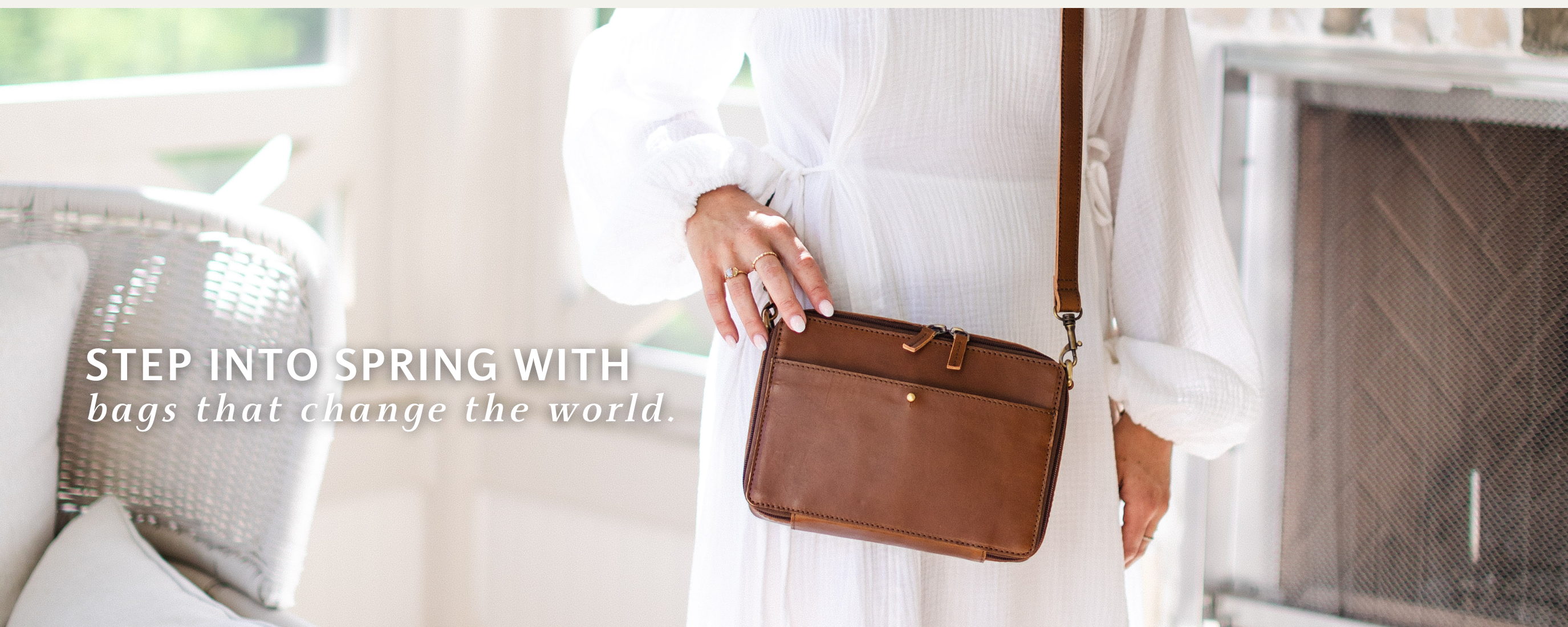 Person holding a brown leather bag with text 'Step into Spring with bags that change the world' in a bright room.