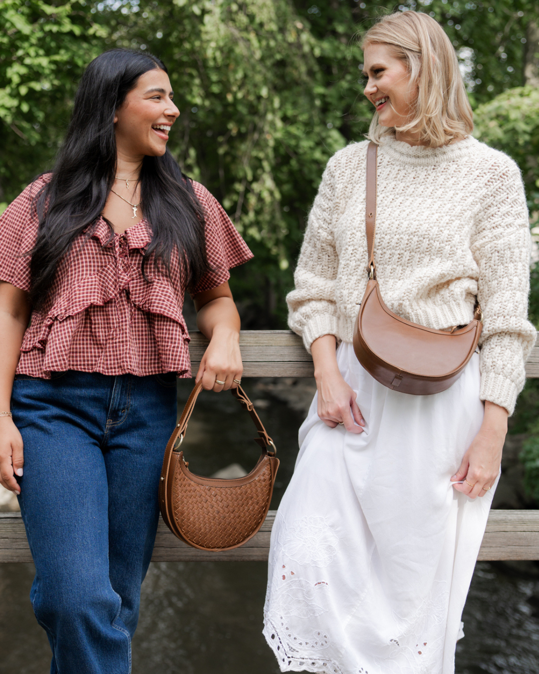Two women standing outdoors, smiling and holding handbags.