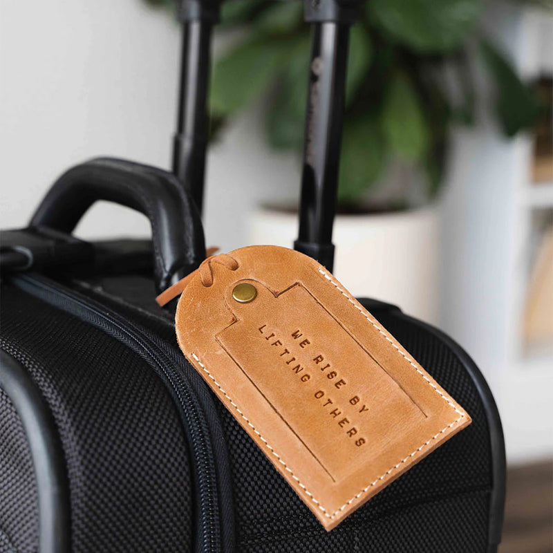 Leather luggage tag securely attached to a suitcase, featuring an embossed message that supports small businesses.