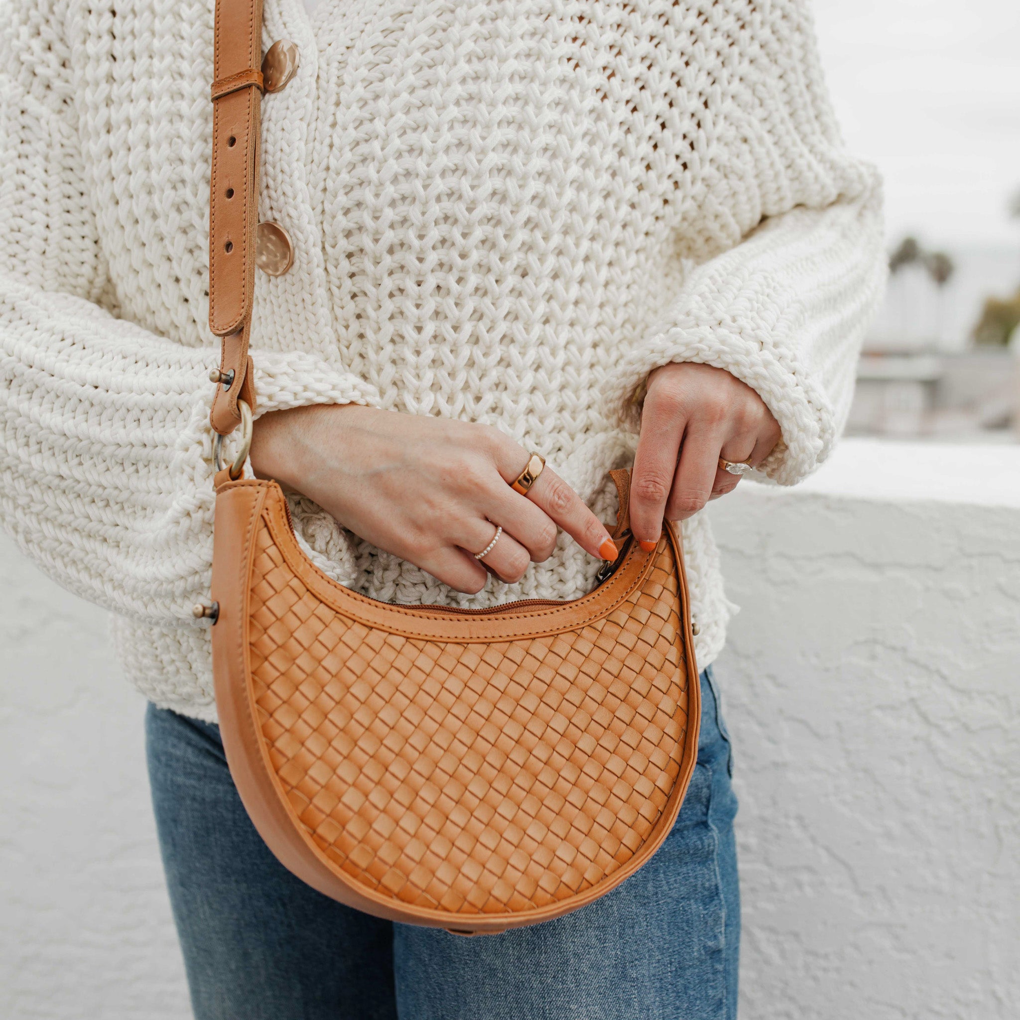 Person holding a woven brown handbag with a blurred background