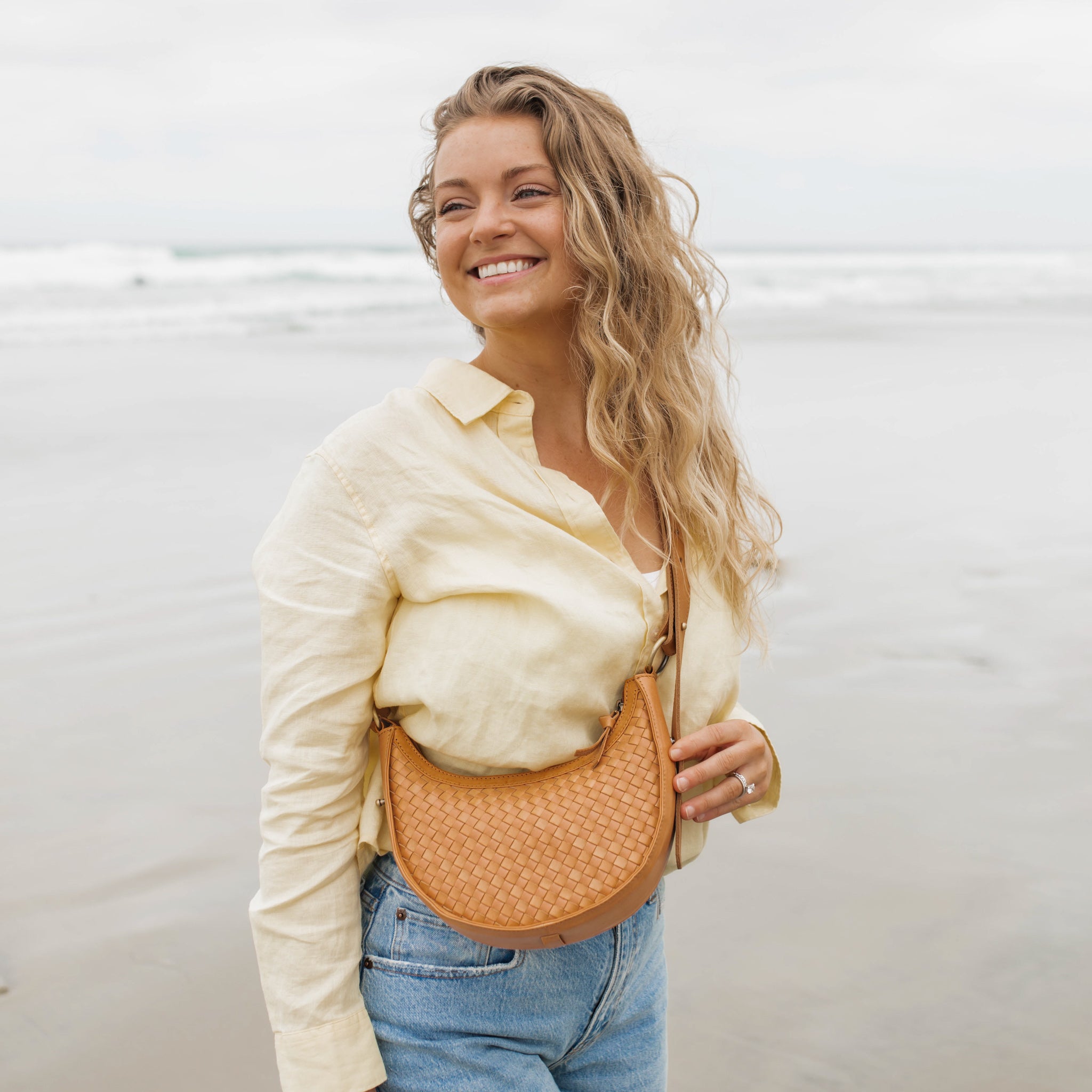 Woman holding a tan leather handbag against a light background