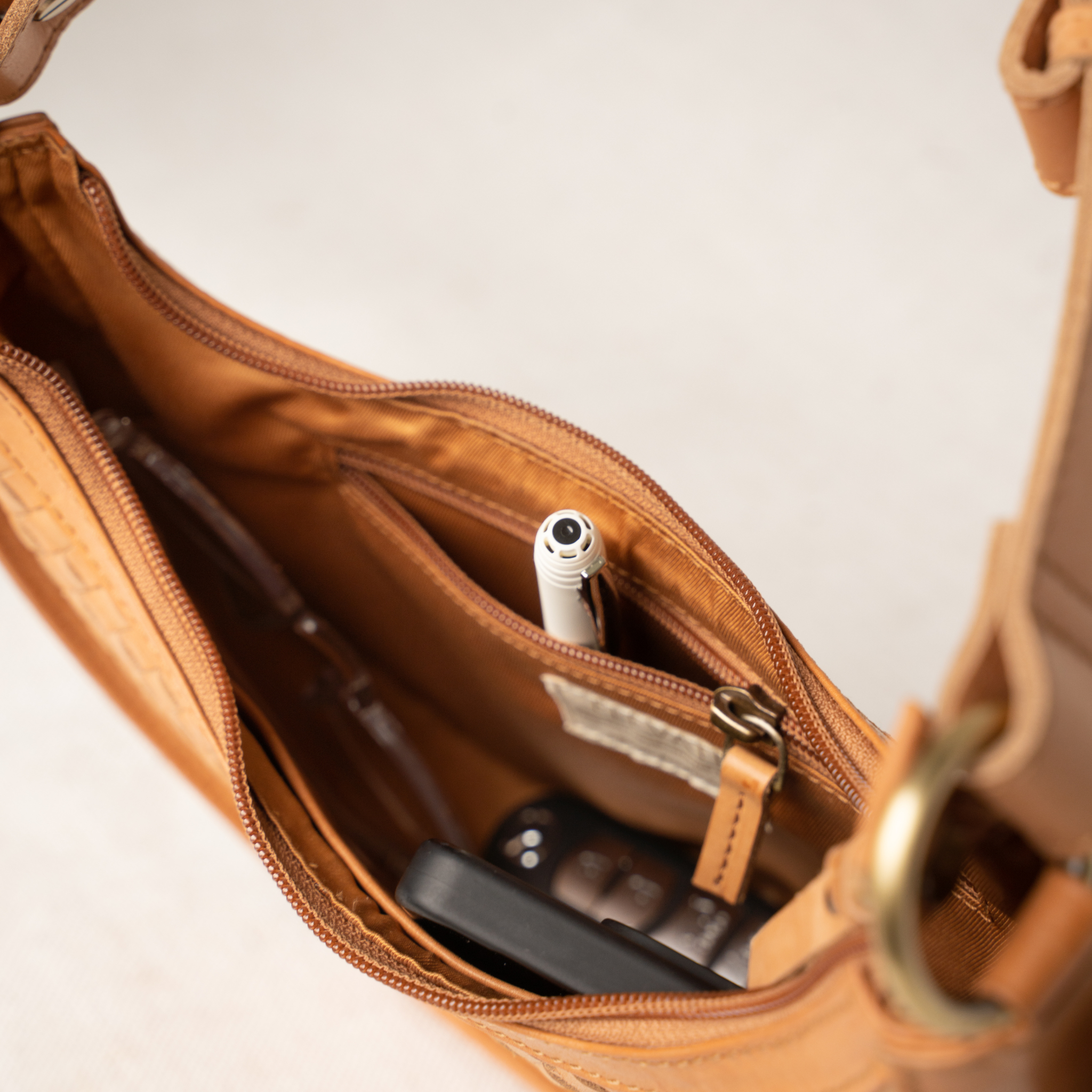 Brown leather handbag with a pen and phone inside on a light background