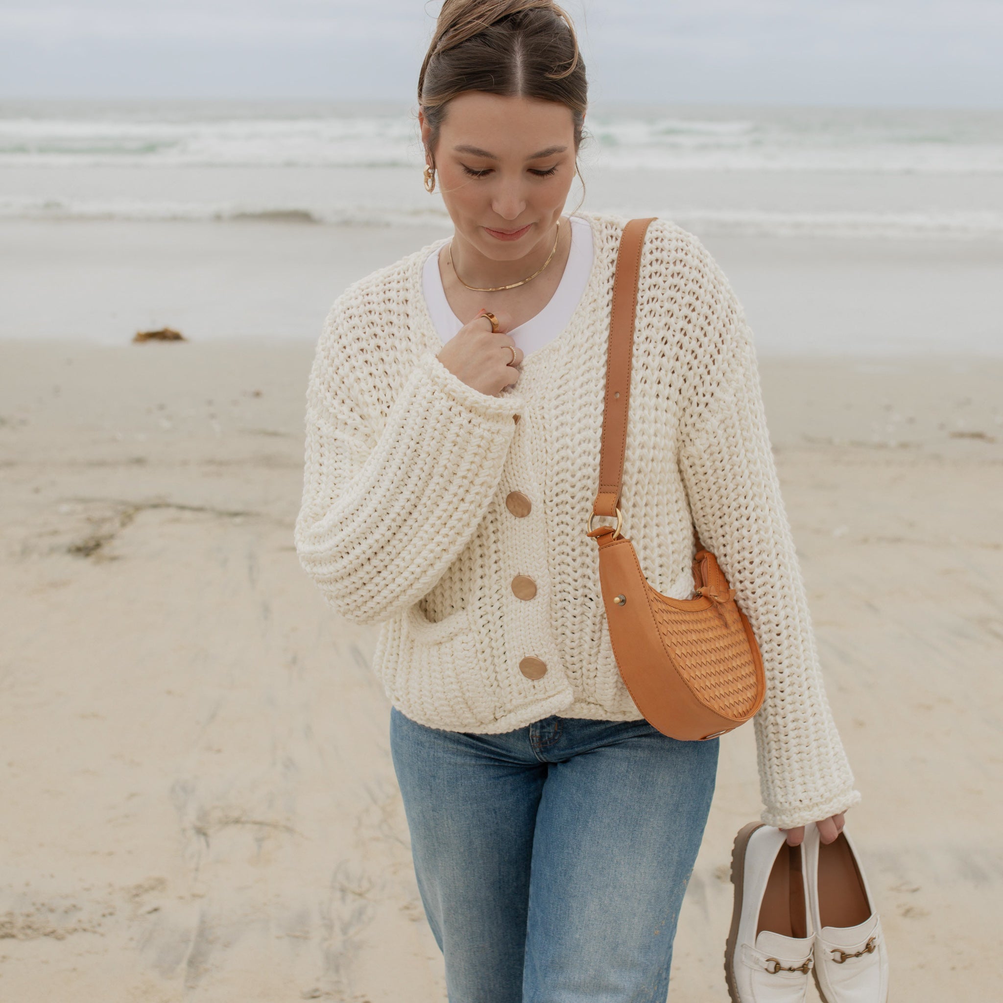 Woman wearing a cream cardigan and blue jeans on a beach