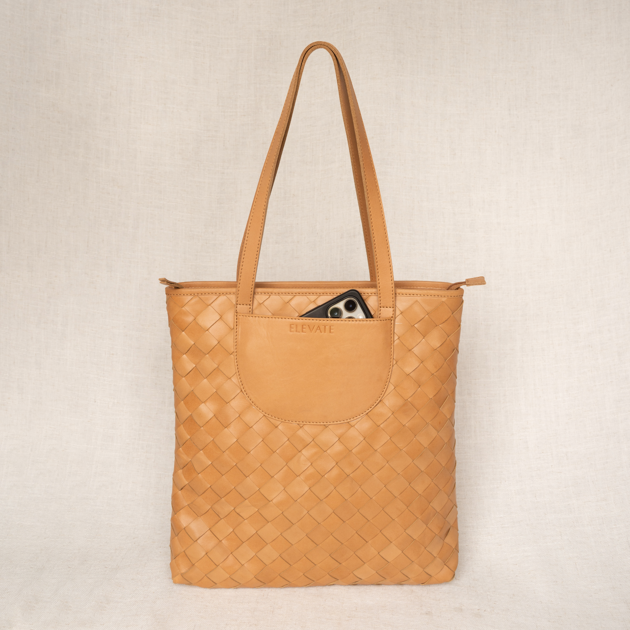 Front view of the Shirin Woven Leather Tote by Elevate, designed in handwoven leather with a smartphone tucked in.