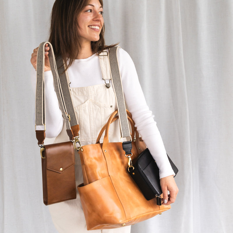 Woman smiling while wearing the Woven Crossbody Bag Strap by Elevate, carrying multiple bags, exhibiting its versatility and chic design.