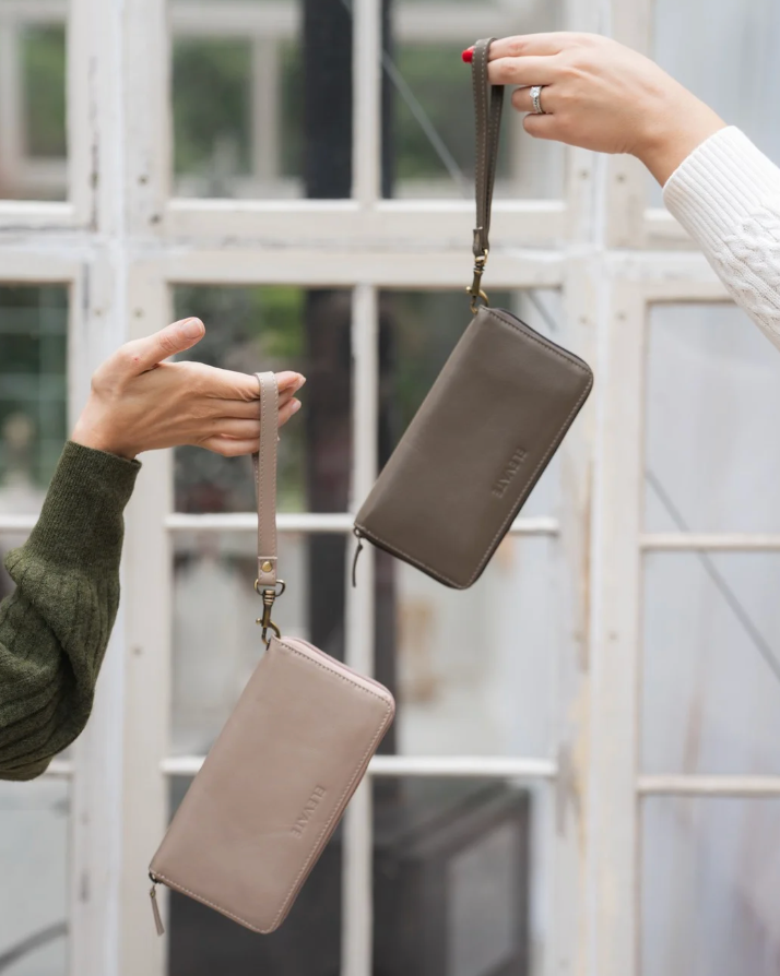 Two hands exchanging two beige leather wallets with a blurred background
