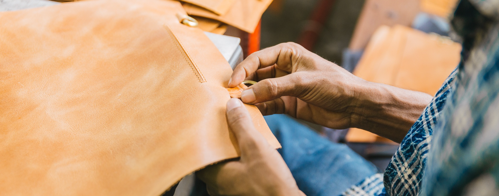 A close up photo of artisan hands working with a piece of our full-grain, camel leather.