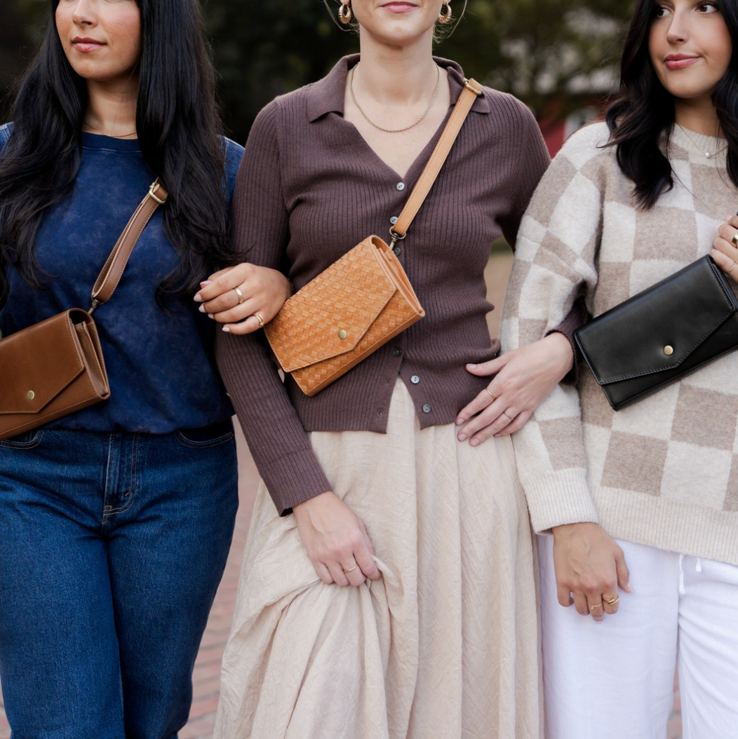 Three women standing together, each holding a different type of handbag.