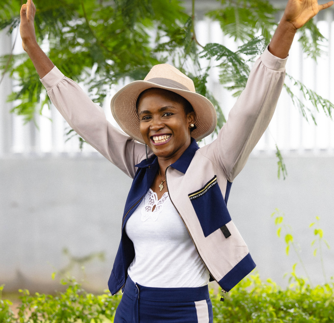 Woman in a hat and jacket with arms raised outdoors