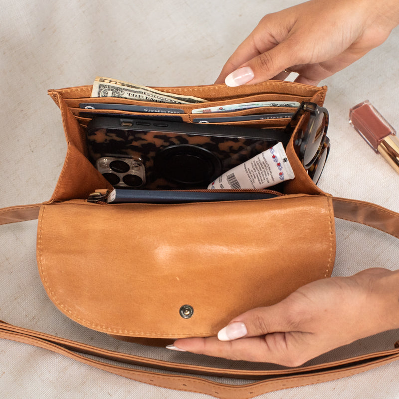 The Solma Leather Fanny Pack arranged with travel essentials like a phone and passport, emphasizing its spacious yet compact design.