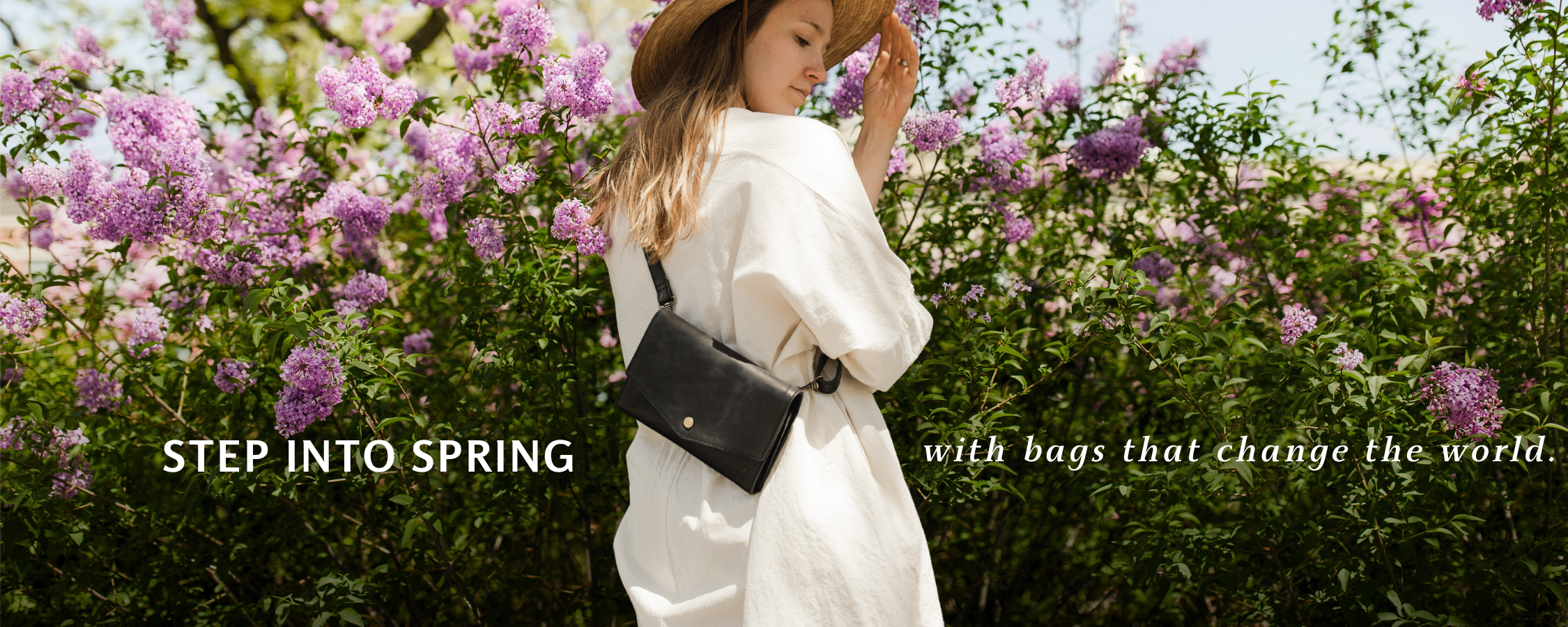 Woman in a white outfit with a black bag standing in front of a lilac bush with text 'Step into Spring with bags that change the world'.